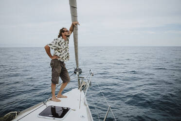 Male sailor standing on bow of sailboat in sea against sky - GMLF00290
