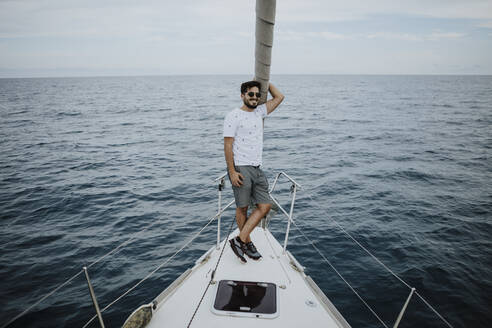 Männlicher Segler mit Sonnenbrille auf dem Bug eines Segelboots im Meer - GMLF00291