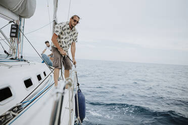 Sailors removing bumpers on sailboat in sea against sky - GMLF00293