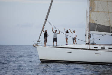 Happy friends waving while standing on sailboat in sea - GMLF00294