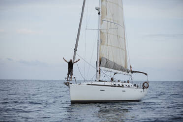 Weiblicher Segler mit erhobenen Armen auf einem Segelboot im Meer stehend - GMLF00295