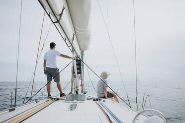 Friends looking at view while sailing on sailboat against sky - GMLF00300