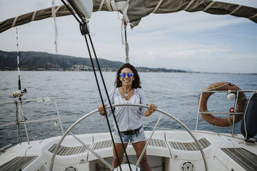Happy female sailor wearing sunglasses driving sailboat on sea - GMLF00302