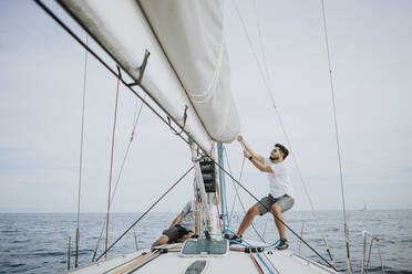 Sailor maneuvering setting the mainsail in sailboat against sky - GMLF00303