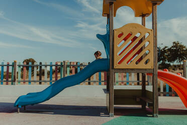 Baby-Mädchen spielen auf Rutsche auf dem Spielplatz gegen bewölkten Himmel - EYF08630