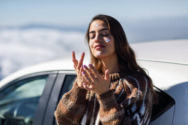 Junge Frau trägt im Winter Feuchtigkeitscreme auf das Gesicht auf - EYF08638