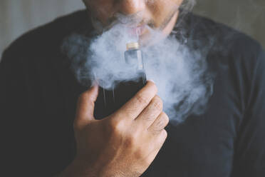 Mittelteil eines Mannes, der eine elektronische Zigarette raucht - EYF08643