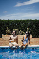 Couple with beer glasses sitting at pool edge - OCMF01367