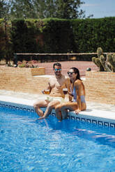 Couple with beer glasses sitting at pool edge - OCMF01368