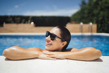 Smiling woman with sunglasses at poolside - OCMF01374