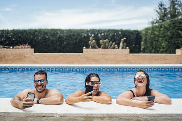Laughing friends during pool party using smartphones - OCMF01377