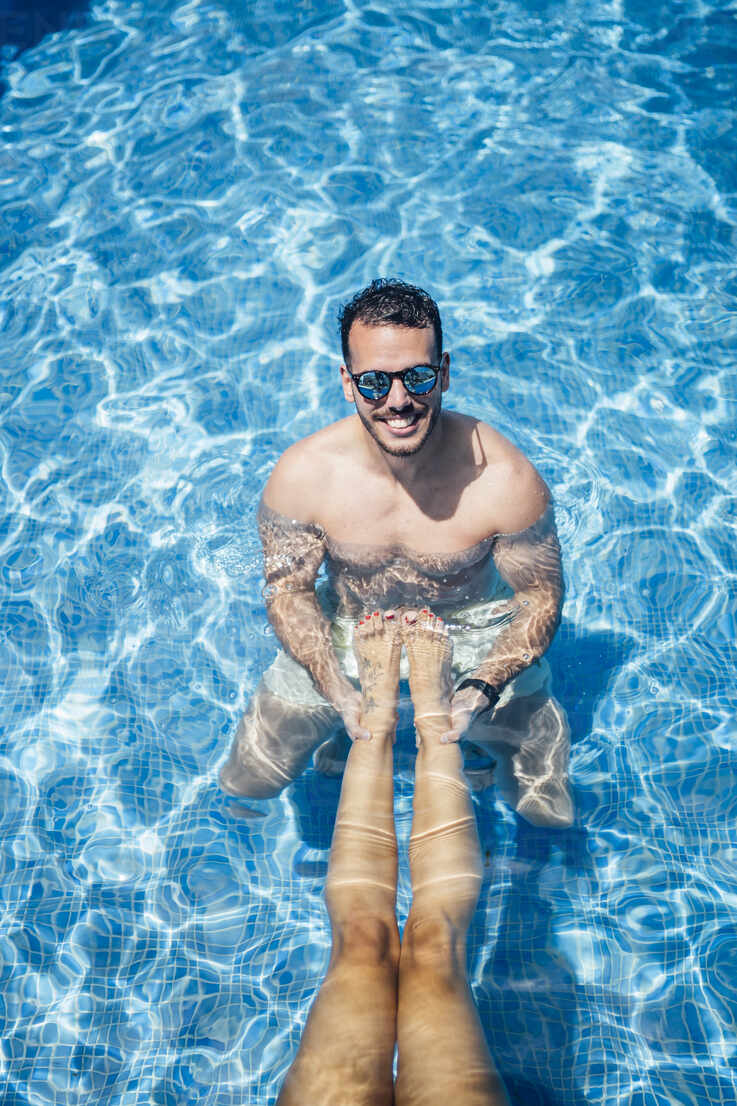 Man with sunglasses holding legs of woman in swimming pool stock photo
