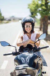 Motorradfahrerin mit Sonnenbrille auf dem Motorrad sitzend - OCMF01388