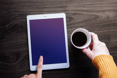 Cropped Hände der Frau hält Kaffeetasse, während mit digitalen Tablet auf Holztisch zu Hause - EYF08733