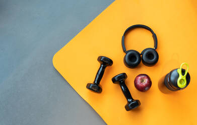 Directly Above Shot Of Apple By Dumbbell And Headphones On Mat - EYF08801