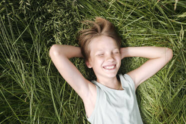 Portrait of happy boy with eyes closed lying on a meadow in summer - EYAF01179