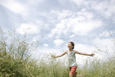 Porträt eines fröhlichen Jungen, der mit ausgestreckten Armen auf einem Feld läuft - EYAF01181