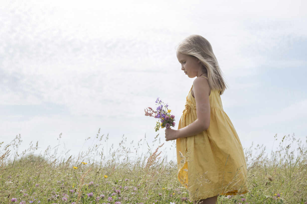 Blond little girl wearing yellow dress standing on a meadow with