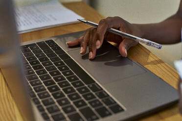 Abgeschnittene Hand einer Frau, die einen Laptop auf dem Tisch benutzt, während sie zu Hause studiert - VEGF02398
