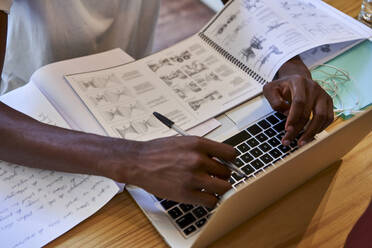 Close-up of young man with books using laptop on table at home - VEGF02405