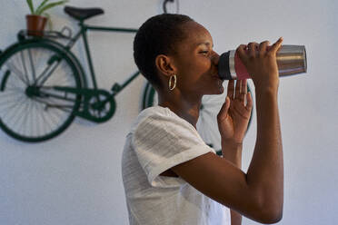 Close-up of young woman drinking water while standing against wall at home - VEGF02410