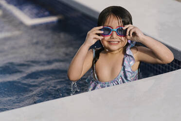 Porträt eines grinsenden kleinen Mädchens mit Schwimmbrille im Schwimmbecken - EGAF00308