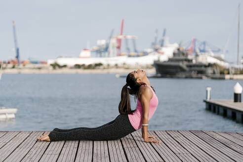 Woman practicing cobra pose on pier against sea at harbor - EGAF00319