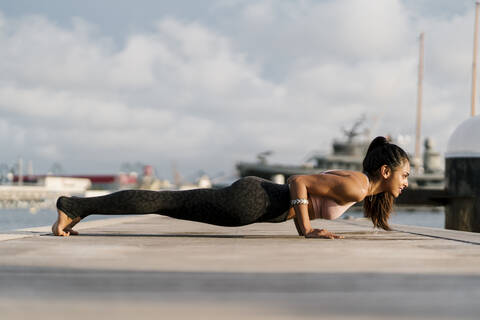 Female athlete practicing four-limbed staff pose on pier at harbor stock photo