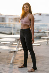 Smiling female athlete standing on pier against clear sky during sunset - EGAF00348