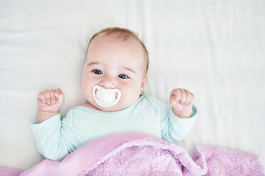 Portrait of baby girl with pacifier lying on bed - KIJF03122