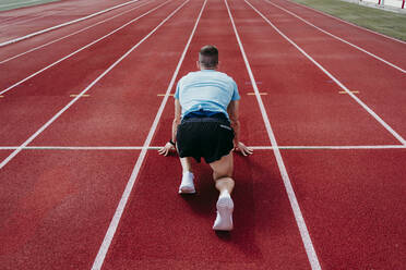 Male athlete in starting position on tartan track - EBBF00223