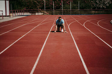 Male athlete in starting position on tartan track - EBBF00229