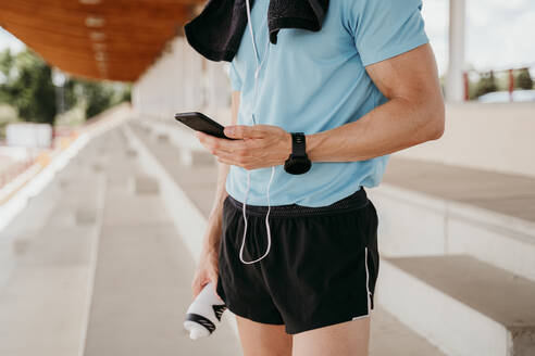 Männlicher Sportler überprüft sein Smartphone auf der Tribüne im Stadion - EBBF00238