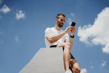 Männlicher Sportler, der eine Pause macht und sein Smartphone überprüft - EBBF00257