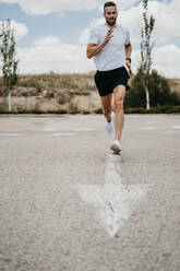 Male athlete running with arrow sign on the road - EBBF00260