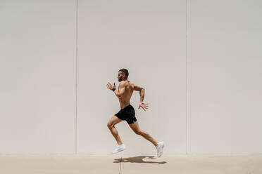 Barechested male athlete running along a wall - EBBF00261