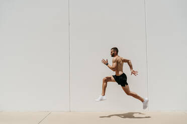 Männlicher Athlet mit nacktem Oberkörper, der gegen eine Wand springt - EBBF00262