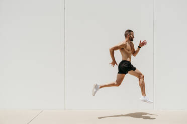 Barechested male athlete jumping at a wall - EBBF00263