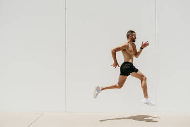 Männlicher Athlet mit nacktem Oberkörper, der gegen eine Wand springt - EBBF00263