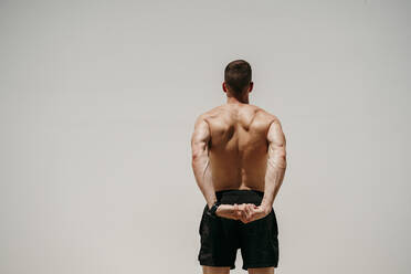 Männlicher Athlet mit nacktem Oberkörper beim Dehnen in der Sonne - EBBF00266