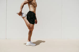 Männlicher Athlet mit nacktem Oberkörper beim Dehnen in der Sonne - EBBF00268