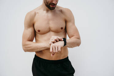 Barechested male athlete checking smartwatch - EBBF00270