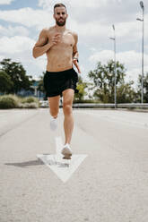 Barechested male athlete running with arrow sign on the road - EBBF00272