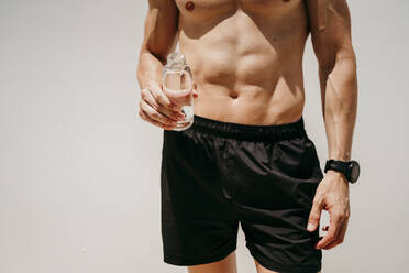 Männlicher Athlet mit nacktem Oberkörper, der eine Wasserflasche hält - EBBF00273