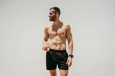 Männlicher Athlet mit nacktem Oberkörper, der eine Wasserflasche hält - EBBF00274