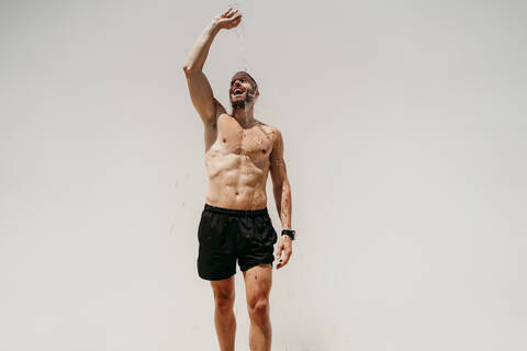 Männlicher Athlet mit nacktem Oberkörper, der sich Wasser über seinen Körper gießt, lizenzfreies Stockfoto