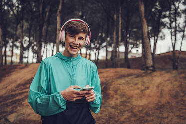 Teenager mit Kopfhörern und Regenmantel im Wald - ACPF00764