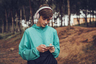 Teenager mit Kopfhörern und Regenmantel im Wald - ACPF00766