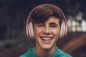 Teenager with headphones wearing raincoat in the woods - ACPF00770