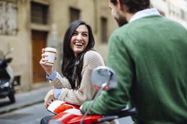 Glückliche Frau mit Kaffee in der Hand, die ihren Freund anschaut, während sie sich auf die Vespa lehnt - SODF00748